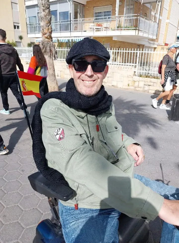Daniel Ruiz smiling on a sunny seafront promenade, wearing a flat cap and sunglasses