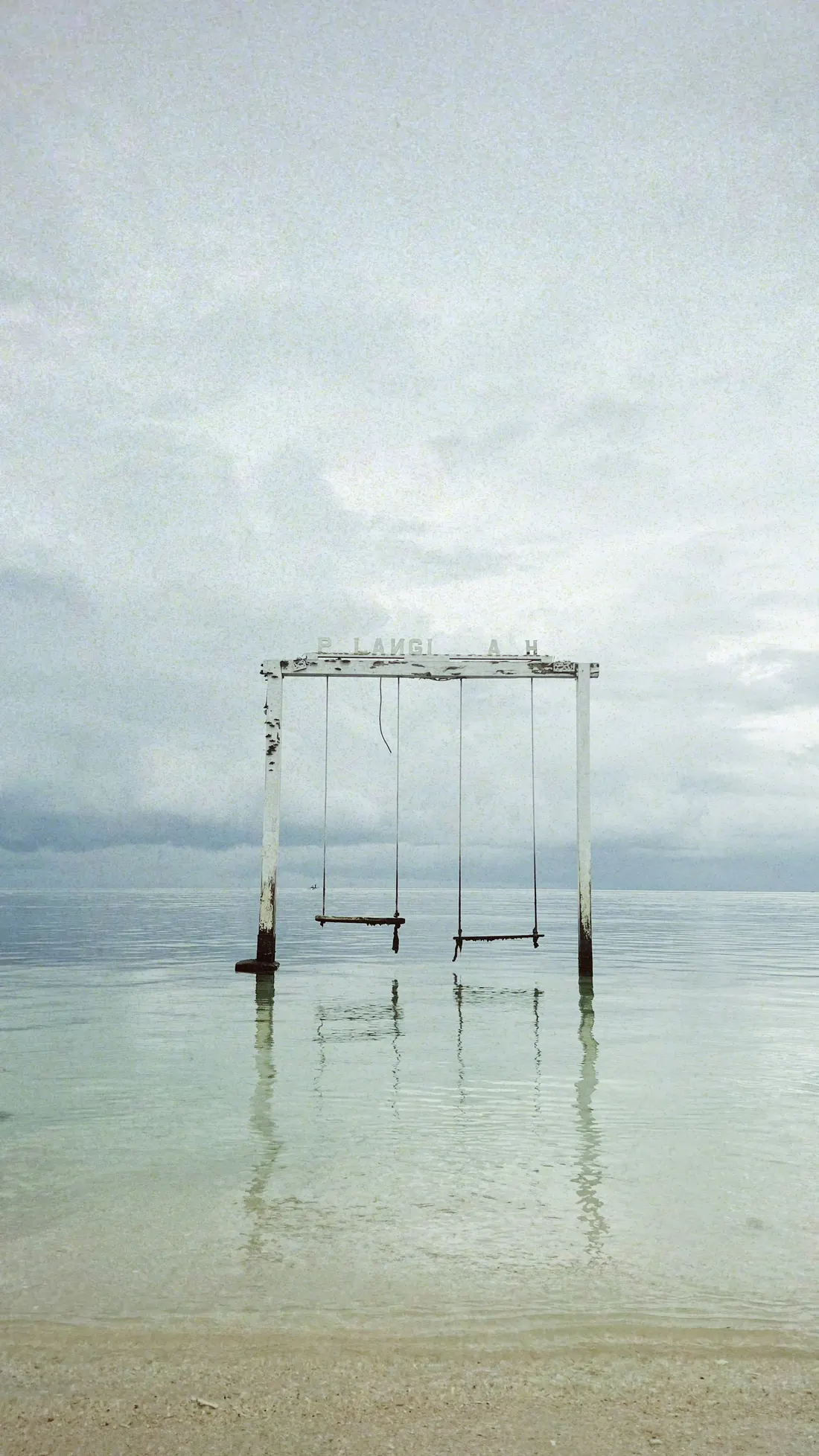A wooden swing standing in the calm shallows of Gili Air
