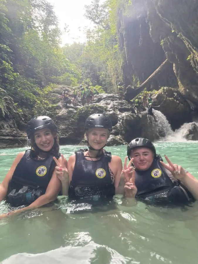 Three guests in helmets and life vests smiling in a turquoise river canyon