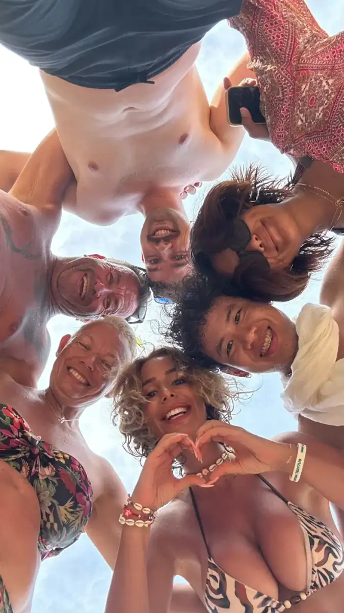 Guests in a circle looking down at the camera, one making a heart with her hands